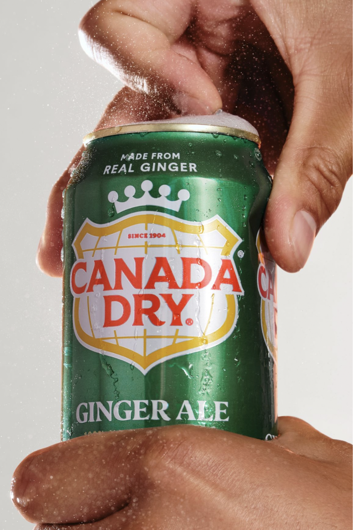 Someone opening a can of Canada Dry on a white background.