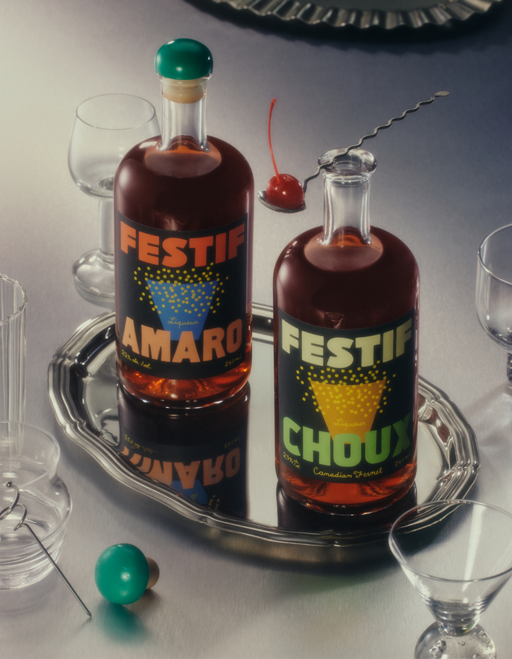 Two bottles of Festif, Amaro and Choux, on a silver platter surrounded by glassware and silverware.