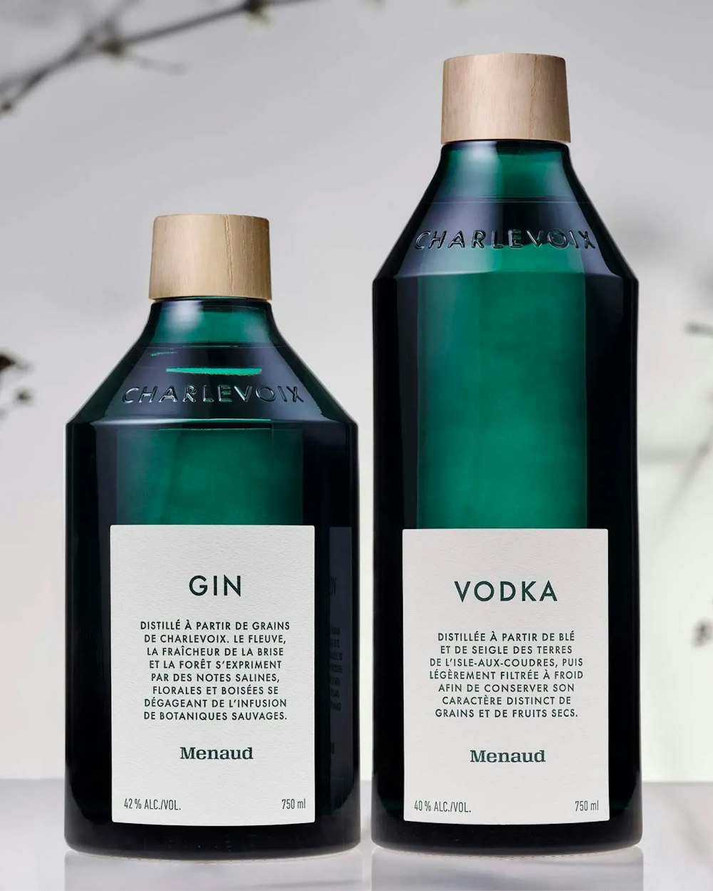 2 bottles of Gin & Vodka of the brand Menaud. The background is a white background with some blurry wild flowers.