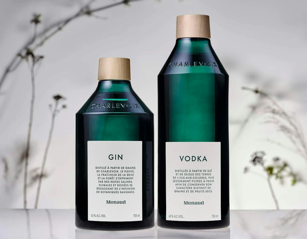 2 bottles of Gin & Vodka of the brand Menaud. The background is a white background with some blurry wild flowers.