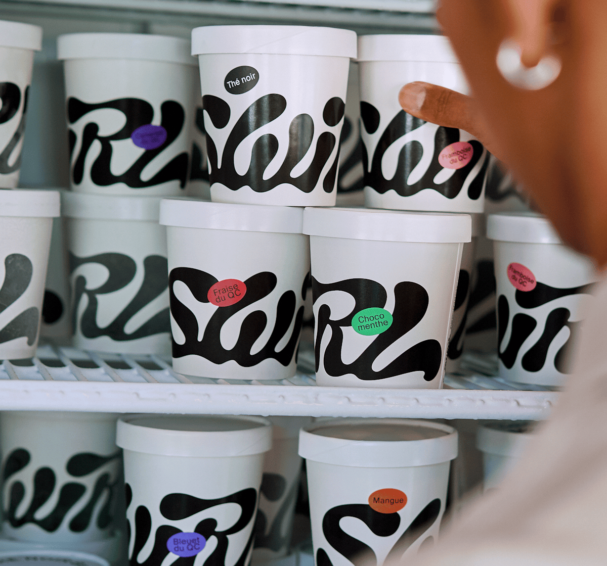A fridge full of Swirl icecream. On the right, the hand and profile of someone taking on of the ice cream pot.