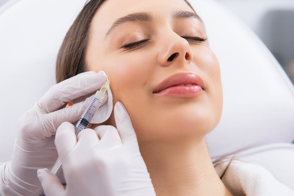 Close-up of a relaxed woman receiving a Botox injection in her cheek.
