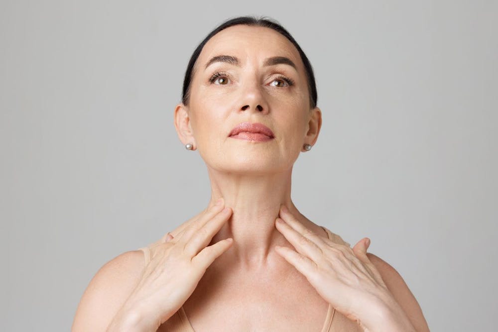 Mature woman examining her neck, representing post-Kybella treatment recovery.
