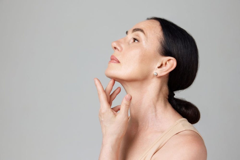 Woman gently touching her throat, reflecting on her Kybella post-treatment care.