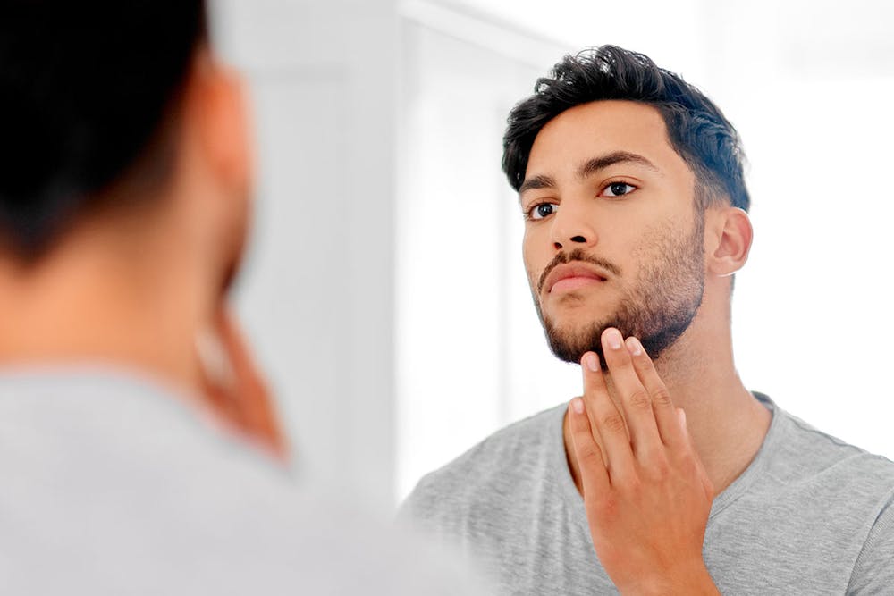 man looking in the mirror after his beard transplant in Miami, FL