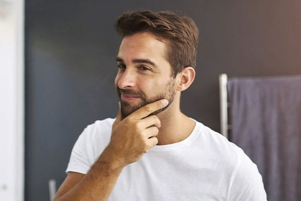 blog-considering-a-beard-transplant-key-things-to-know-first-1 man looking in the mirror after his beard transplantation in Miami, FL