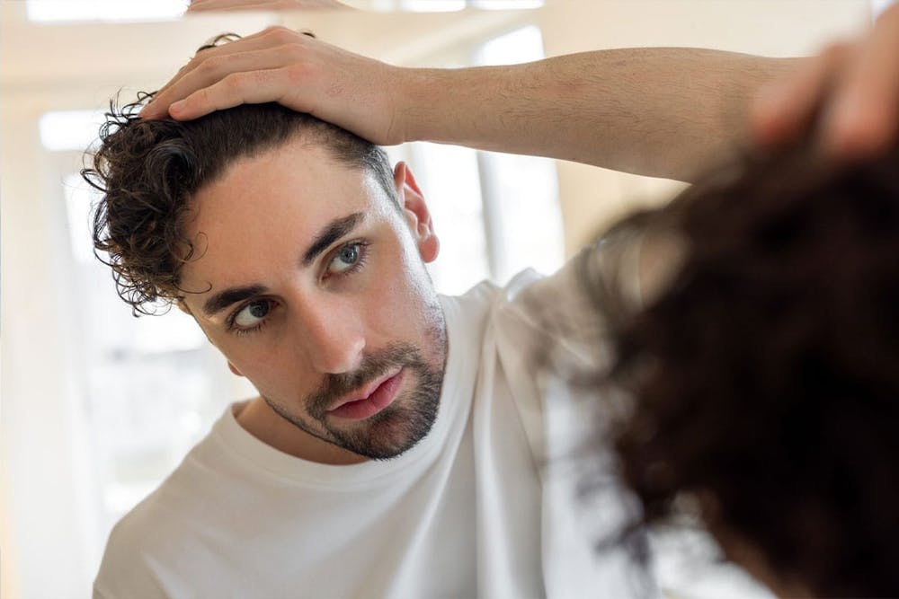 blog-is-there-an-ideal-age-for-a-hair-transplant-1 man looking in the mirror after his hair transplant in Miami, FL