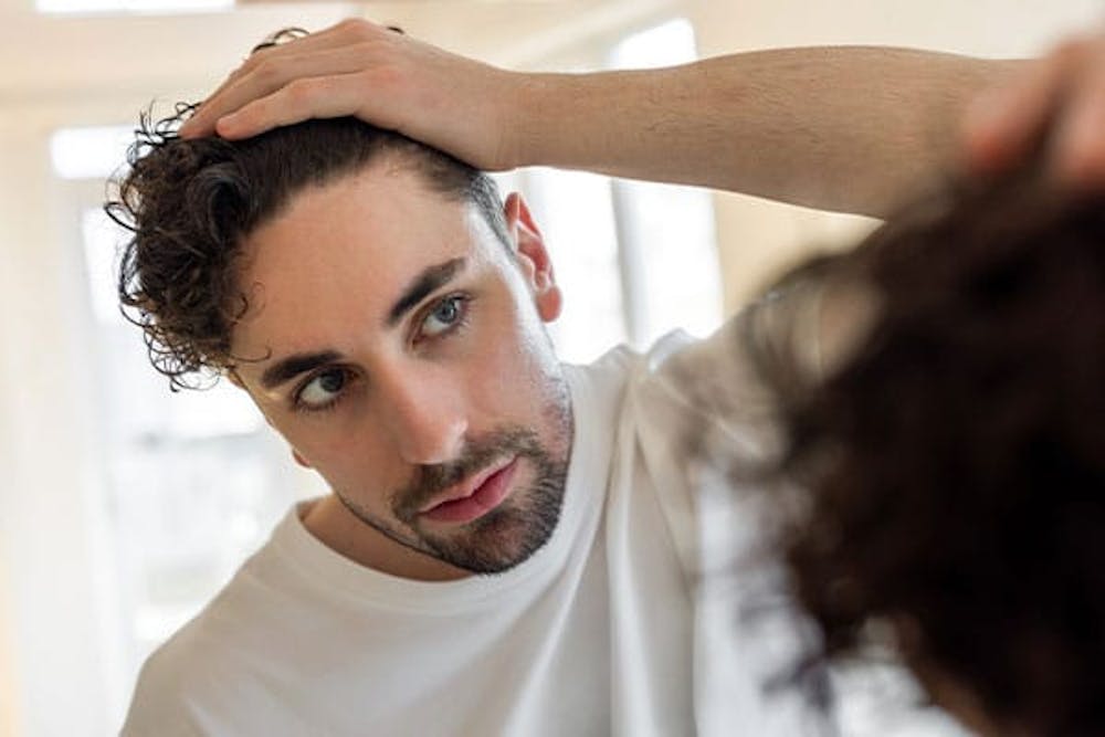 blog-hair-loss-in-20s-is-it-too-early-to-consider-restoration-1 man looking in the mirror before getting hair restoration treatment in Miami, FL