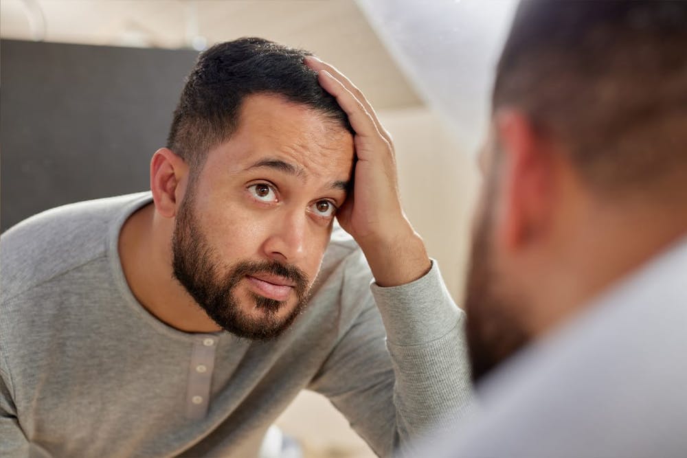 man looking in the mirror after his hair transplant in Miami, FL