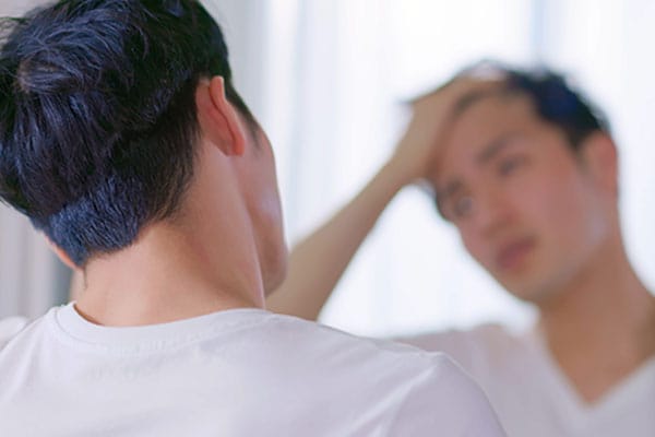 man looking at his hairline in the mirror after his hair transplant in Miami, FL