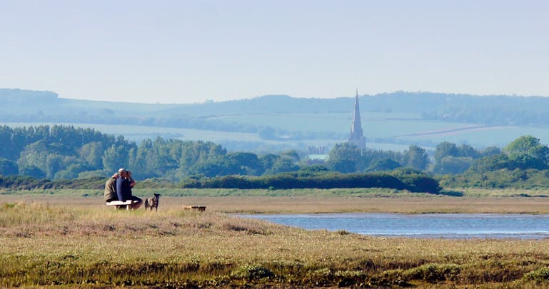 Bird watchers looking out on Pagham Harbour with Chichester Cathedral in the background Image of Bird watchers looking out on Pagham Harbour with Chichester Cathedral in the background