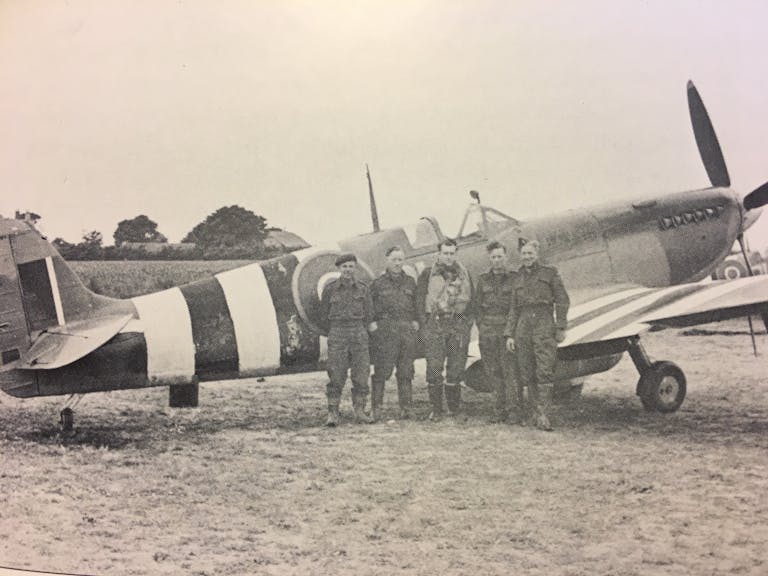 Image of the ALG Selsey airmen alongside a spitfire painted with black and white stripes across its wings and fusalage called Invasion Stripes to fend off friendly fire during the Normandy landings and D-Day 