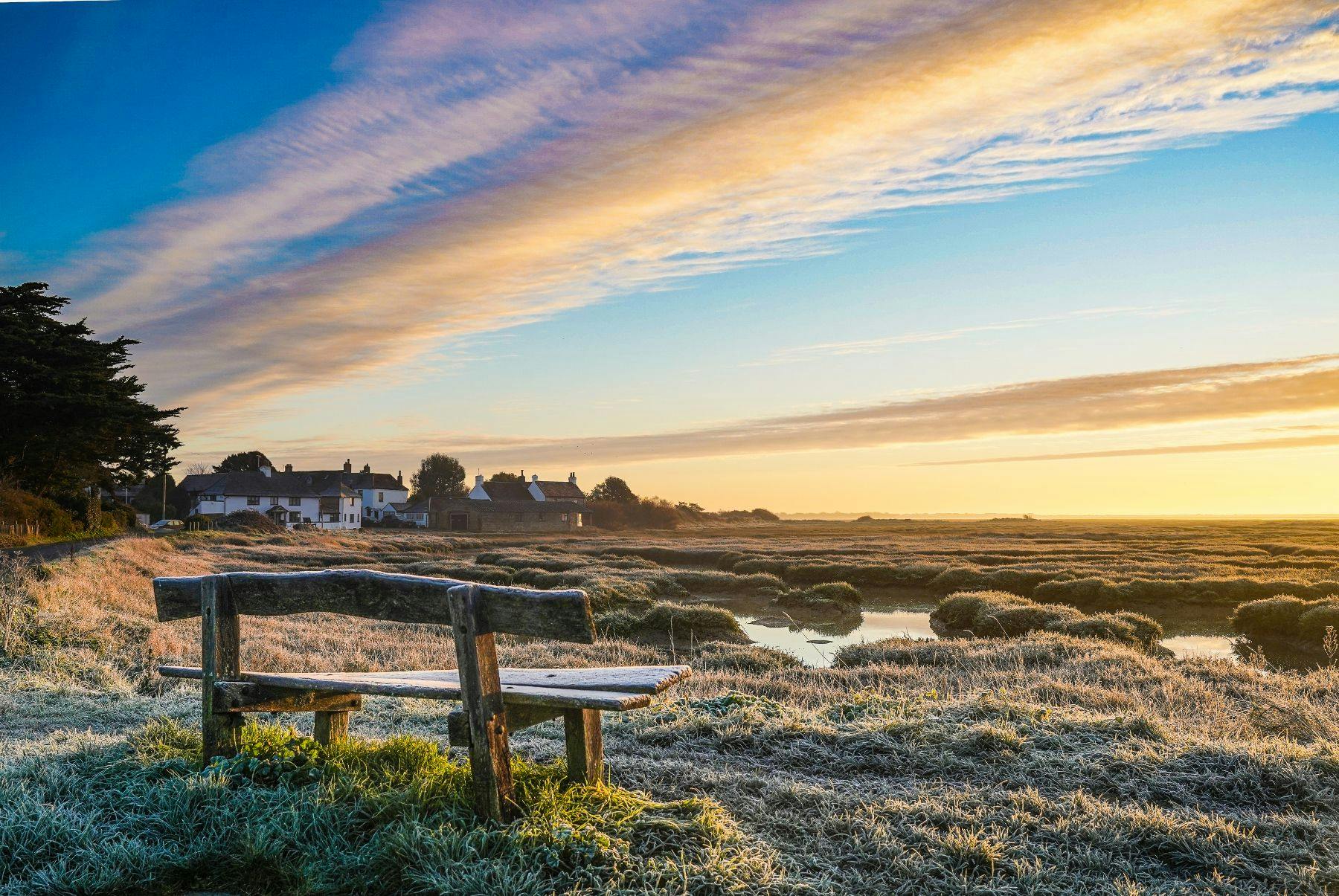 Winter scene of a bench, mudglats and massive skies at Pagham Harbour towards the Crab & Lobster at Sidlesham