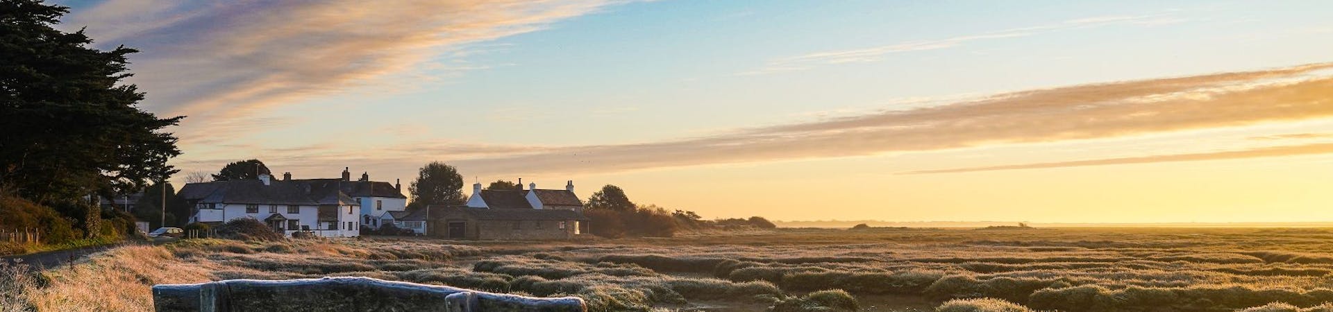 Winter scene of a bench, mudglats and massive skies at Pagham Harbour towards the Crab & Lobster at Sidlesham