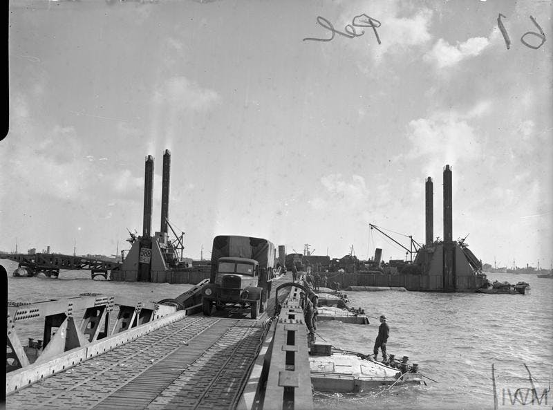 Military vehicle being driven off the Mulberry Harbour along a constructed bridge 