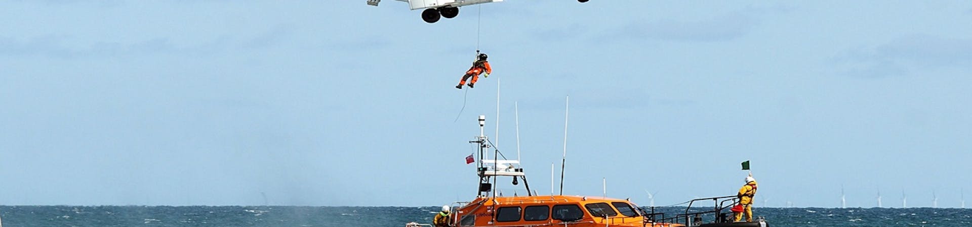 A coastguard helicopter hovers over the RNLI Selsey lifeboat as an individual is hoisted up to the helicopter.  This was part of the display during RNLI Selsey Lifeboat week.