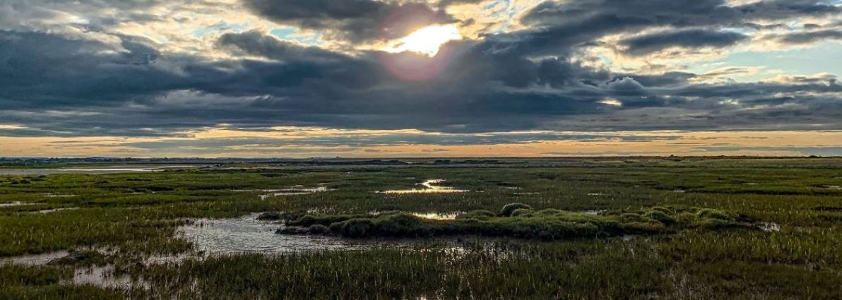 the sun peaking behind the clouds above the mud flats at Church Norton