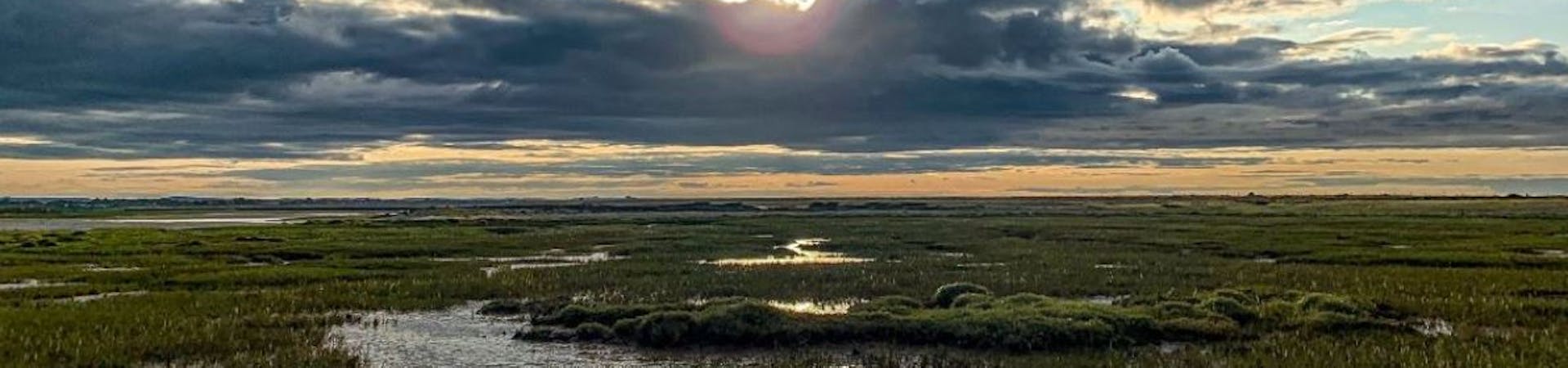 the sun peaking behind the clouds above the mud flats at Church Norton