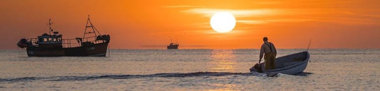 Fishermen heading out for a catch to the backdrop of an orange sunrise, Selsey