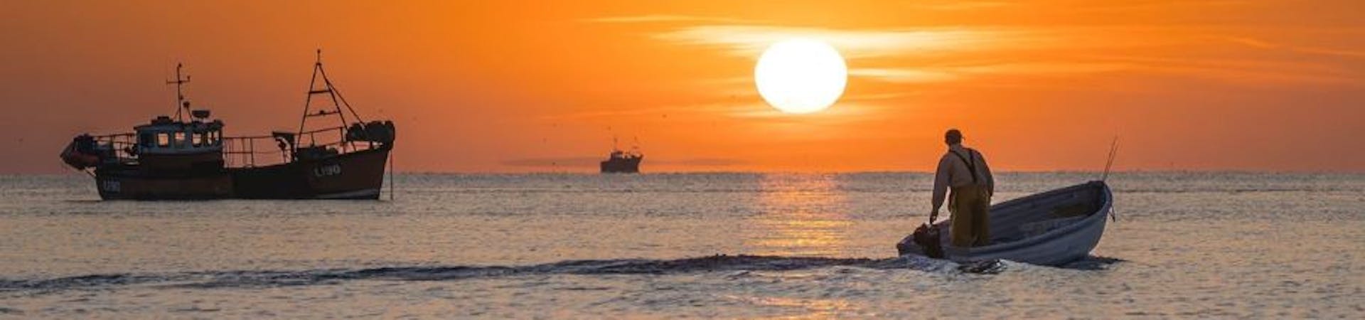 Fishermen heading out for a catch to the backdrop of an orange sunrise, Selsey