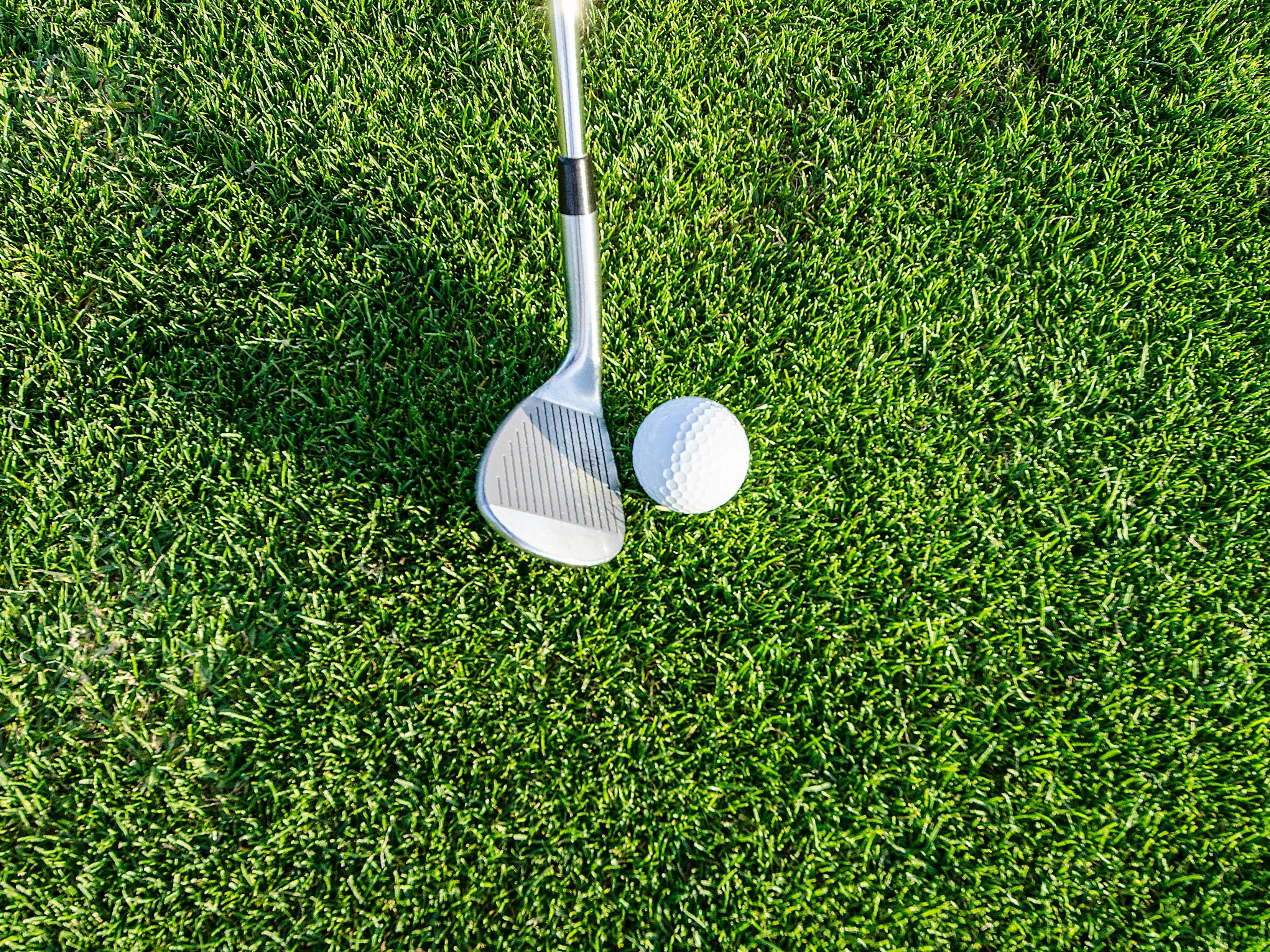 Golf club about to hit ball on green grass