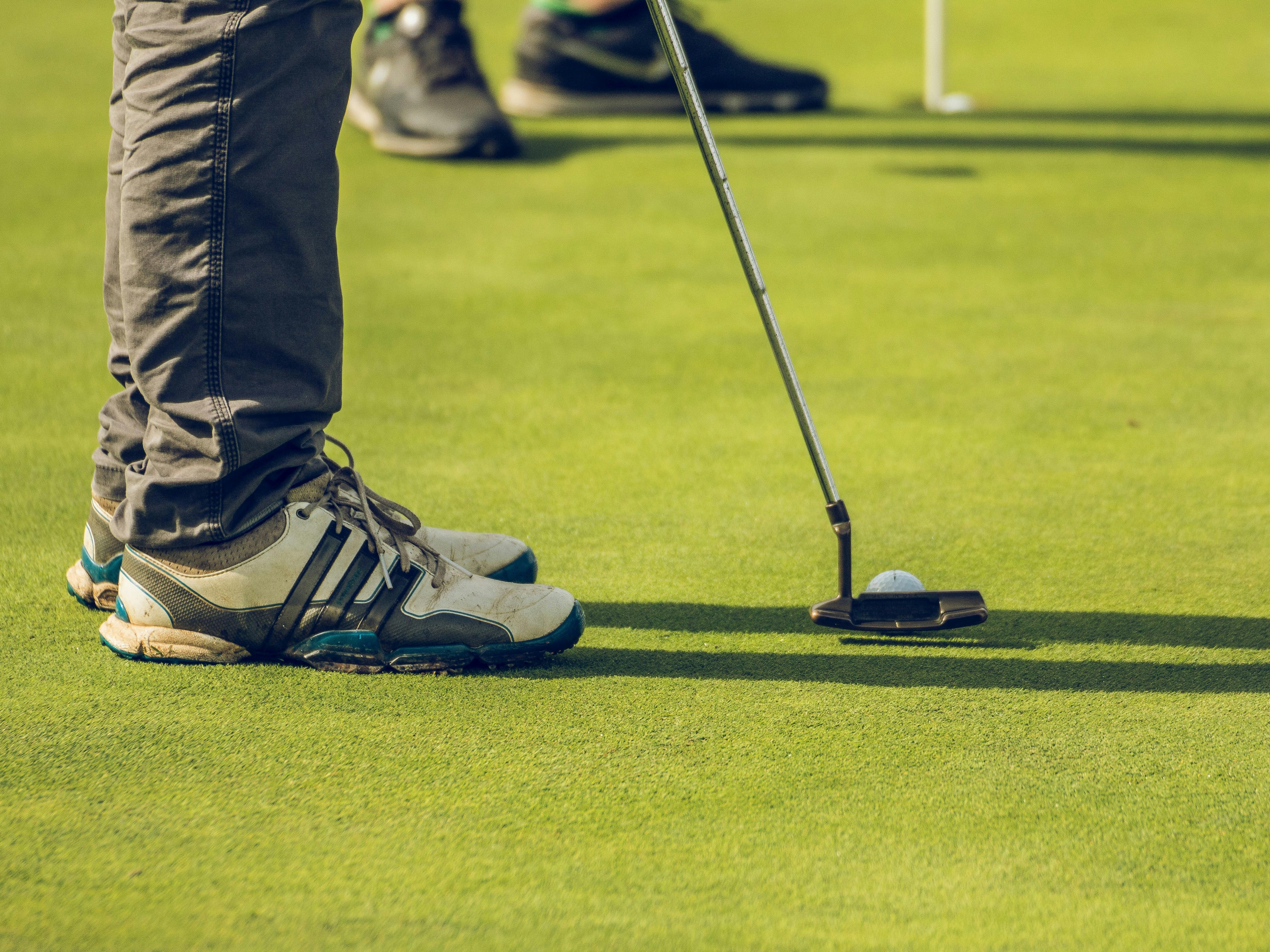 The lower legs and trainers of an individual lining up their putter with the ball