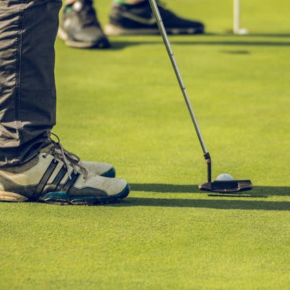 The lower legs and trainers of an individual lining up their putter with the ball