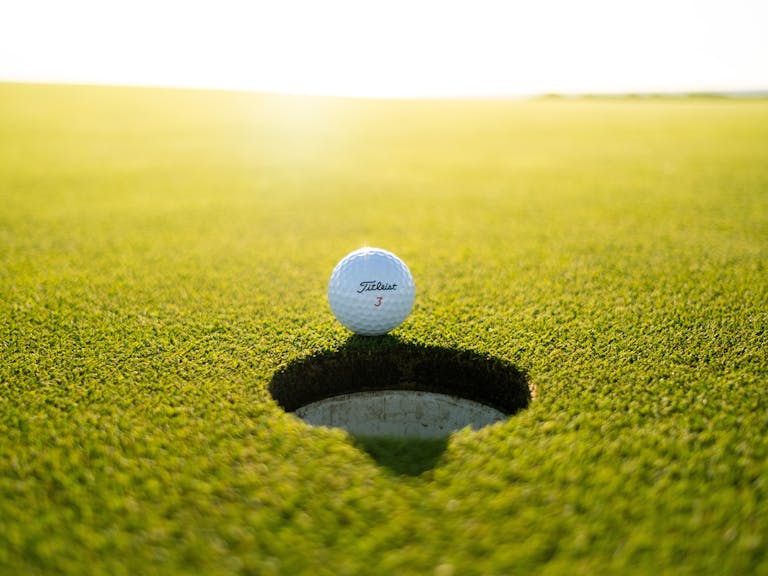 A golf ball teeters on the edge of a hole
