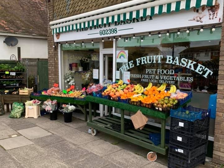 Front of the Fruit Basket Shop with fresh fruit laid out consisting of bannanas, melons, apples, oranges and pinapples 