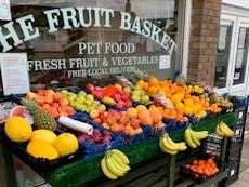 Front of the Fruit Basket Shop with fresh fruit laid out consisting of bannanas, melons, apples, oranges and pinapples 