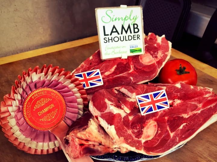 A pair of Scotch Premier Meat Champion winning lamb shoulders displayed on a butchers board with a whole tomato as garnish 