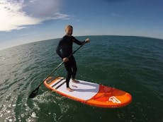 Paddle boarder on an orange and white board, standing upright on it on the sea waters 