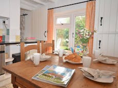 An image of Sea Pinks Cottage in Selsey, the kitchen with dressed table ready for breakfast with fresh croisants with the natural light flooding through the kitch window over looking the lush garden. 