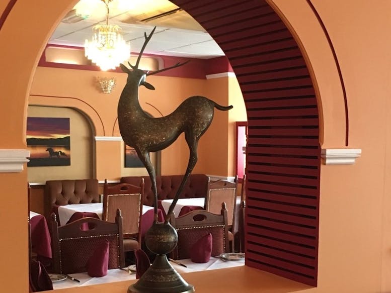 Dining inside of New Magna Tandoori Restaurant A view of the dining area at the New Magna Tandoori Restaurant looking through an arch with a deer scultpture in the foreground