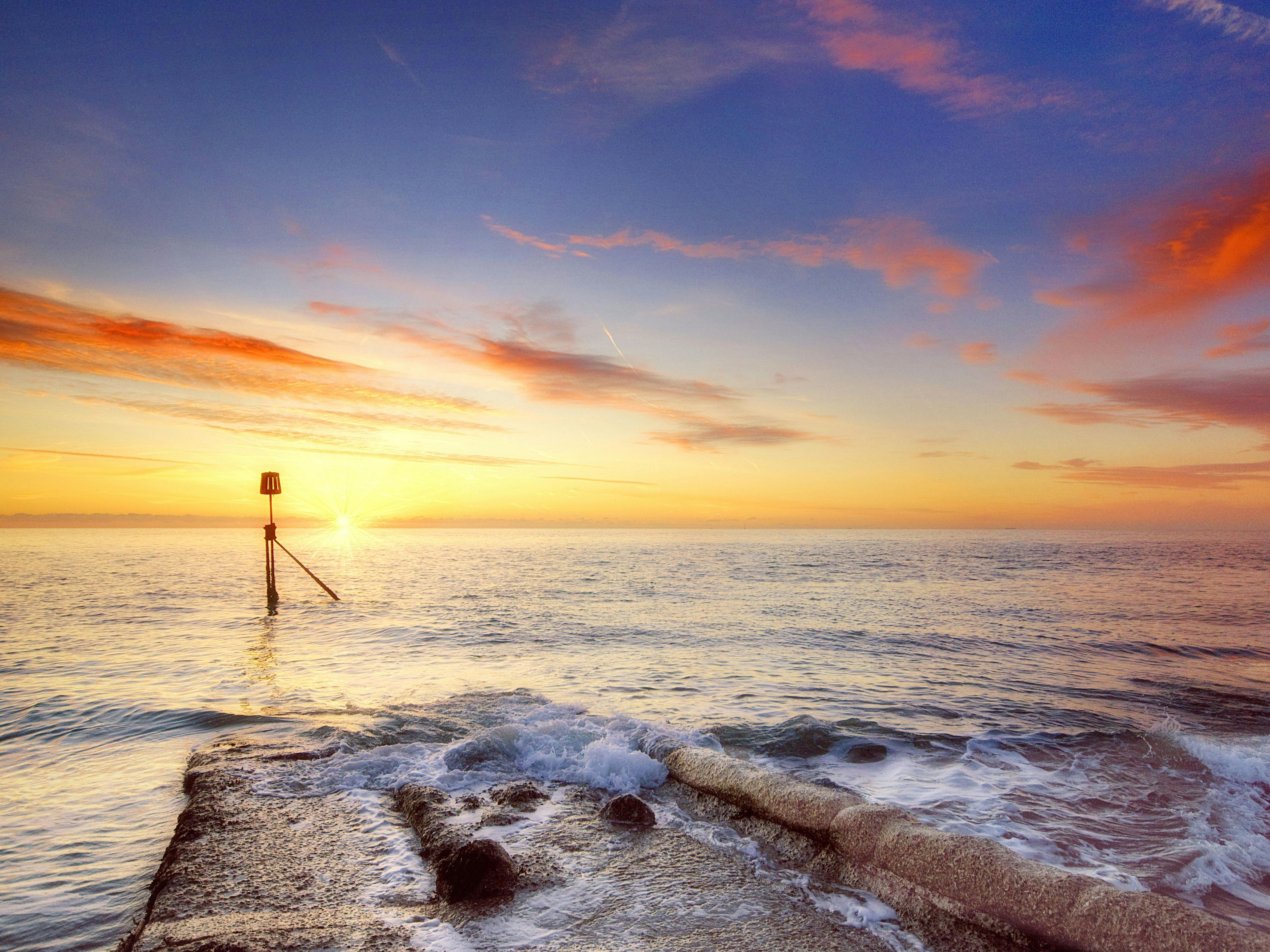 Selsey Bill at sunrise with the reds, oranges and blues of the sky and rolling waves.