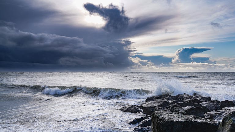 The waves hitting rocks and the clouds take on a majestic formation in the sky