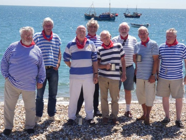 Eight men in striped blue and white tops standing on a beach