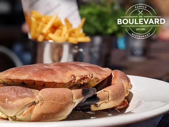 Image of a whole cooked crab on a plate with a metal container of french fries in the background over layed with the logo of the Boulevard restaurant logo