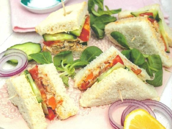 Crab sandwich on white bread, cut into quaters and surrounded by lettuce leaves and red onion slices