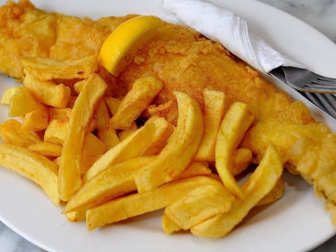 Photograph of fish and chips on a plate with a wedge of lemon on the fish and cutlery to the side