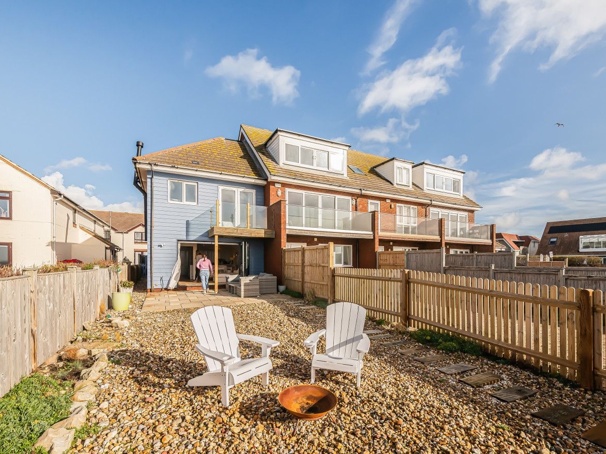 Photogrph of the back of a beachside property with two adirondack style chairs in the gravel garden