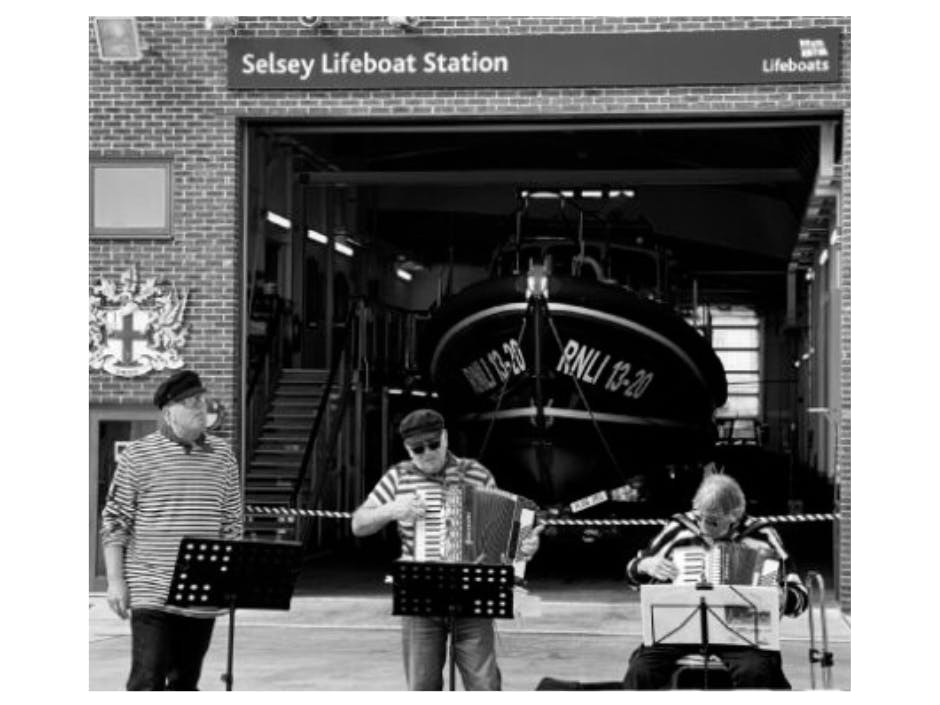 Black and white photograph of The Selsey Shantymen performing outside of Selsey Lifeboat Station