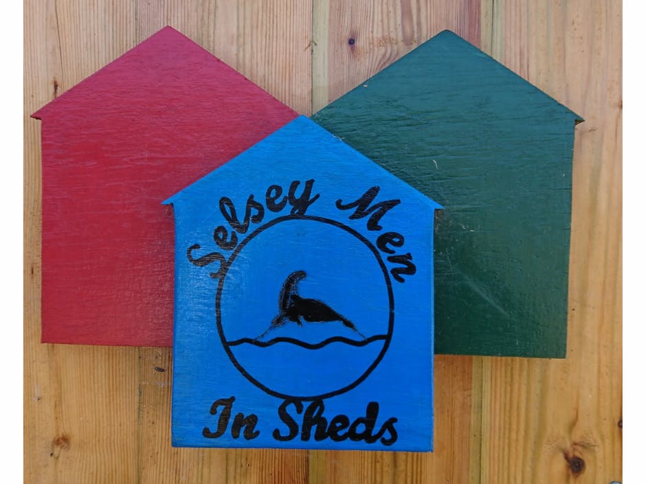 Three shed shapes, one red, one green, one blue. Front blue shed shape states 'Selsey Men In Sheds'