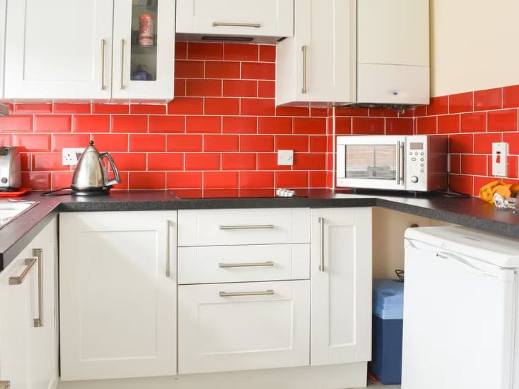 Photograph of a kitchen with red tiles and white cupboard units