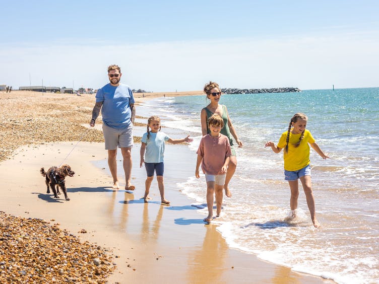 Photograph of a five people, to adults and three children, walking along a beach with a dog