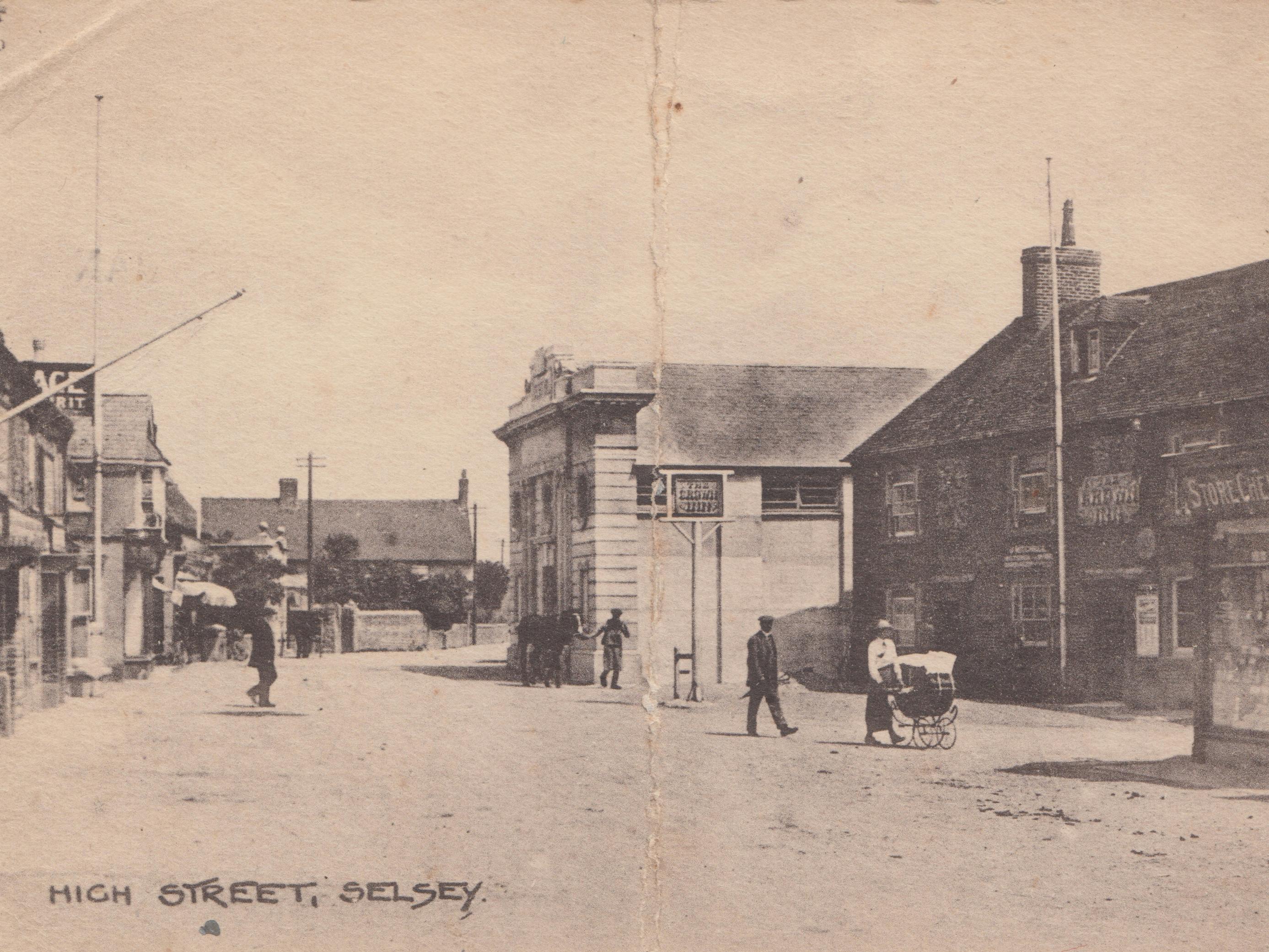 Early 20th Century Postcard Photo in black and white of Selsey High Street with the Pavilion featured back right, the Crown in the foreground and Edwardian dressed residents, one pushing a pram