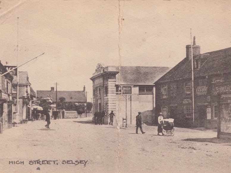 Original Selsey Pavilion Building Early 20th Century Early 20th Century Postcard Photo in black and white of Selsey High Street with the Pavilion featured back right, the Crown in the foreground and Edwardian dressed residents, one pushing a pram