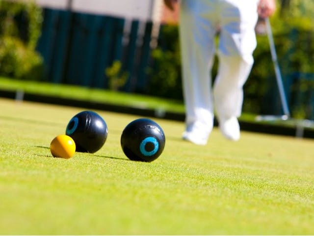 outside bowl game with two black balls and a small yellow ball with a figures legs in the background dressed in white trousers