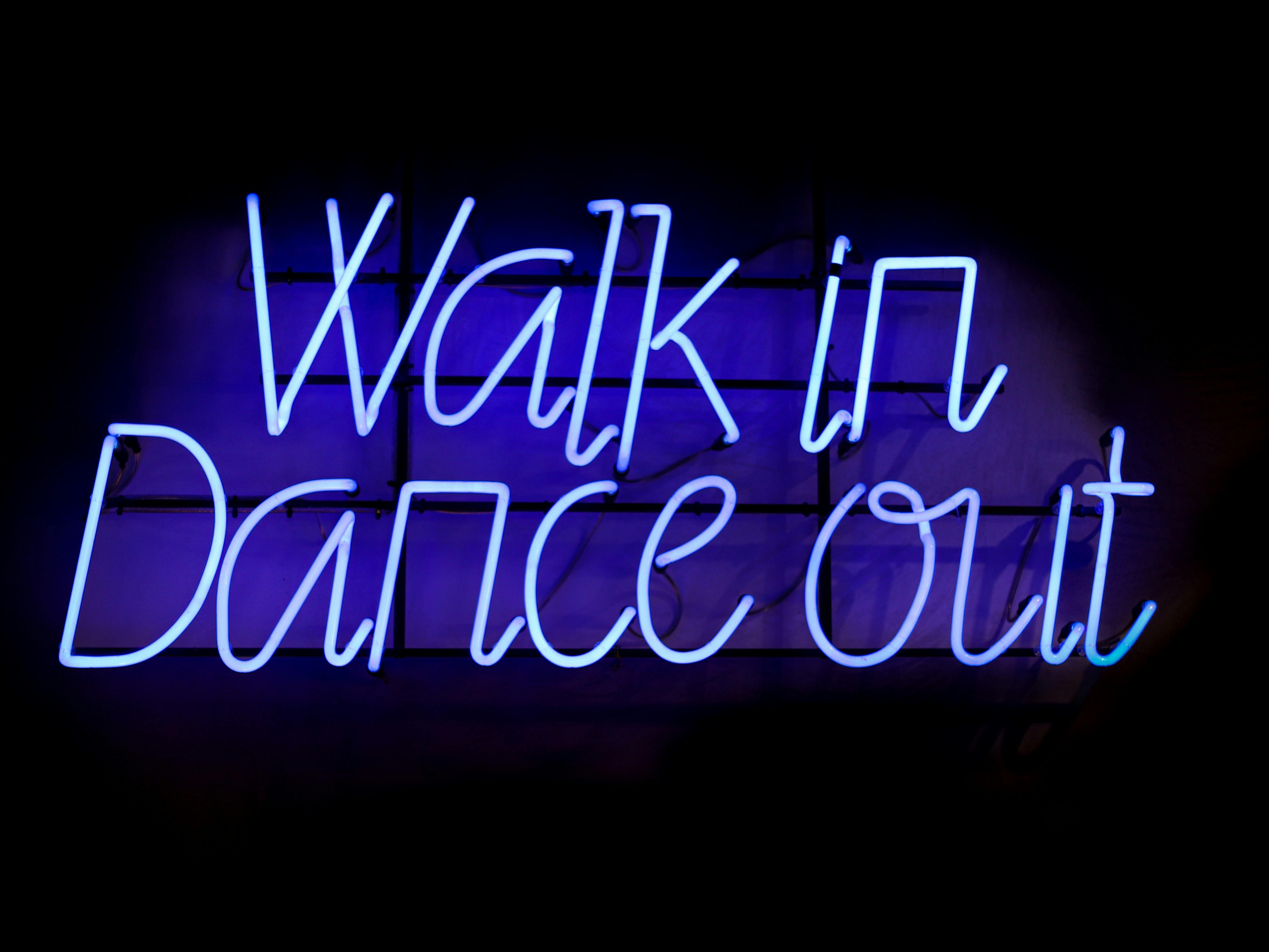 Blue neon light spelling out Walk in Dance out