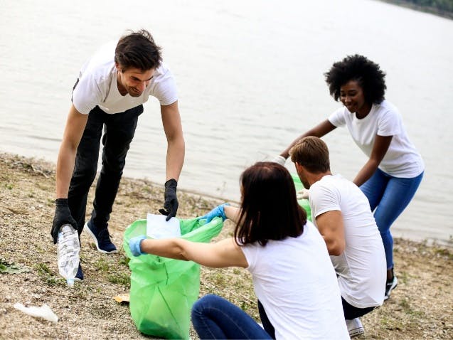 Photograph of four people filling a green plastic bag with rubbish on a beach
